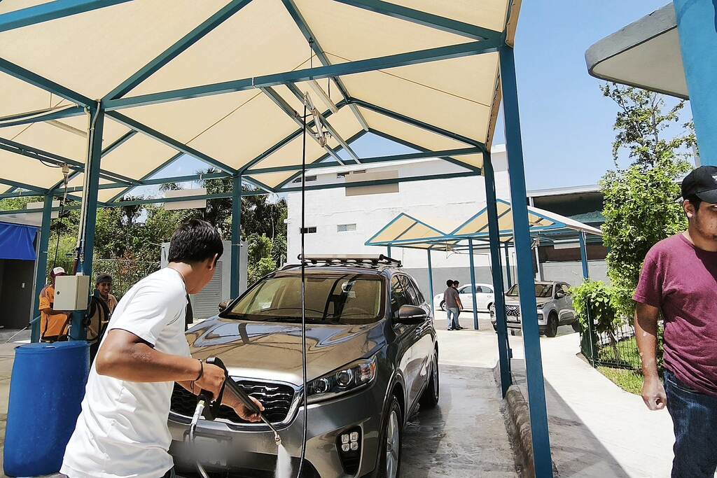 Un lavador enjuaga a presión el frente de una camioneta bajo las lonas de El Arrecife